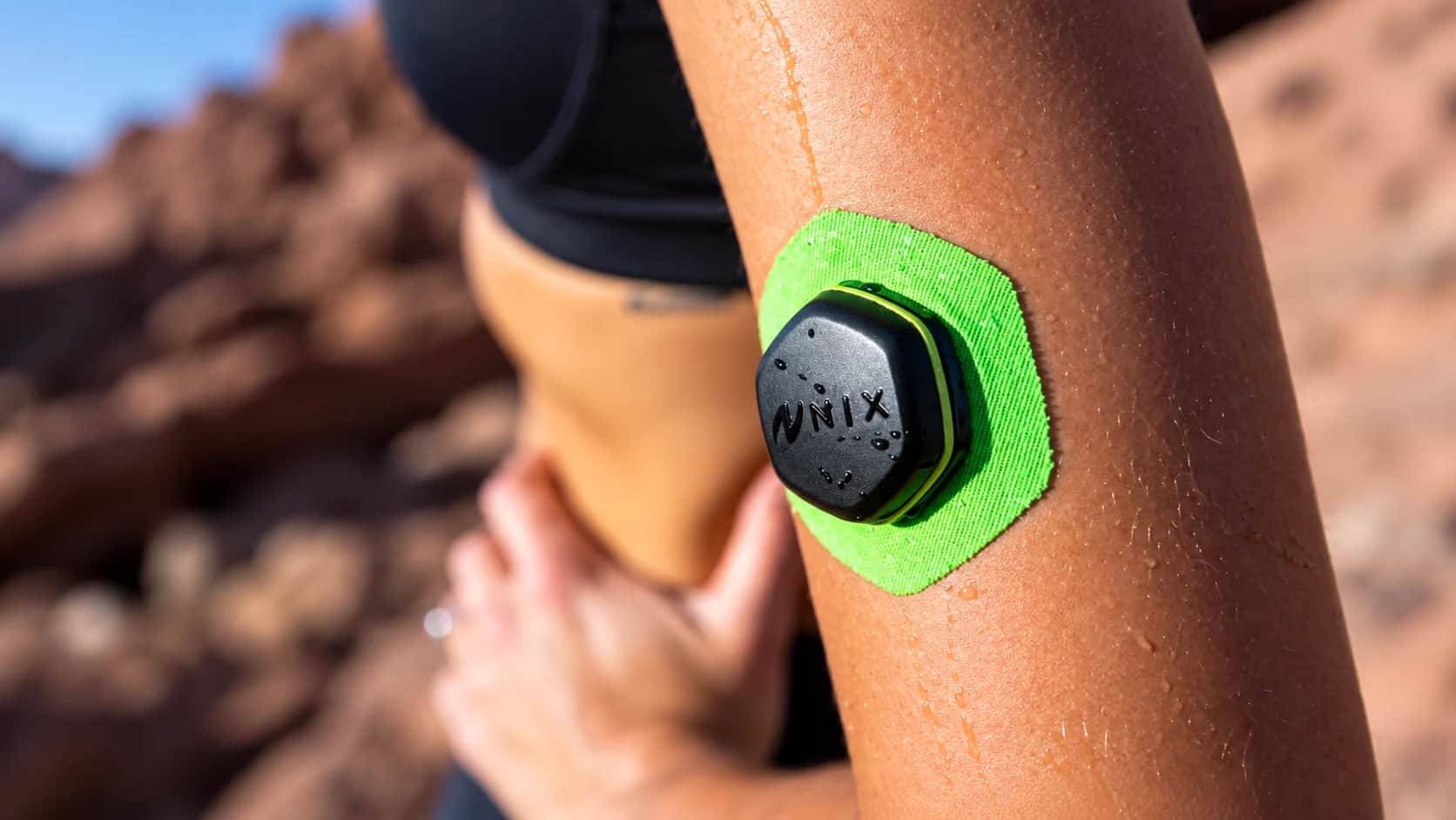 Nix Hydration Biosensor: o sensor que transforma suor em alertas de hidratação Ciclista adulto suado com um biossensor adesivo no bíceps e um celular no guidão exibindo indicadores gráficos de hidratação.